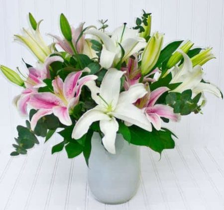 A simply elegant design of white and pink lilies in a sleek white glass urn.