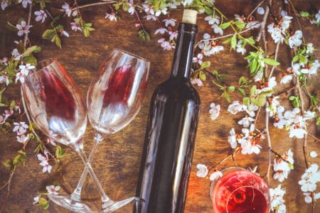 A bottle of wine, glasses with red wine and flowering branch of fruit tree on a wooden background