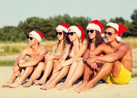 5 young adults sitting on beach wearaing xmas hats