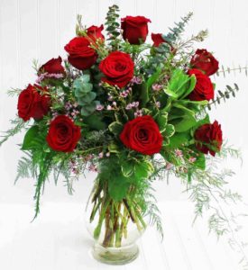 A dozen red roses arranged with garden greens, fragrant eucalyptus and accent flowers are hand-delivered in a fashionable glass vase